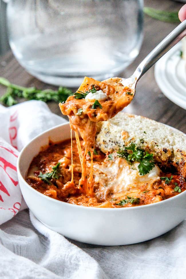 Lasagna Soup in a white bowl with cheese with a spoon serving a bite. 