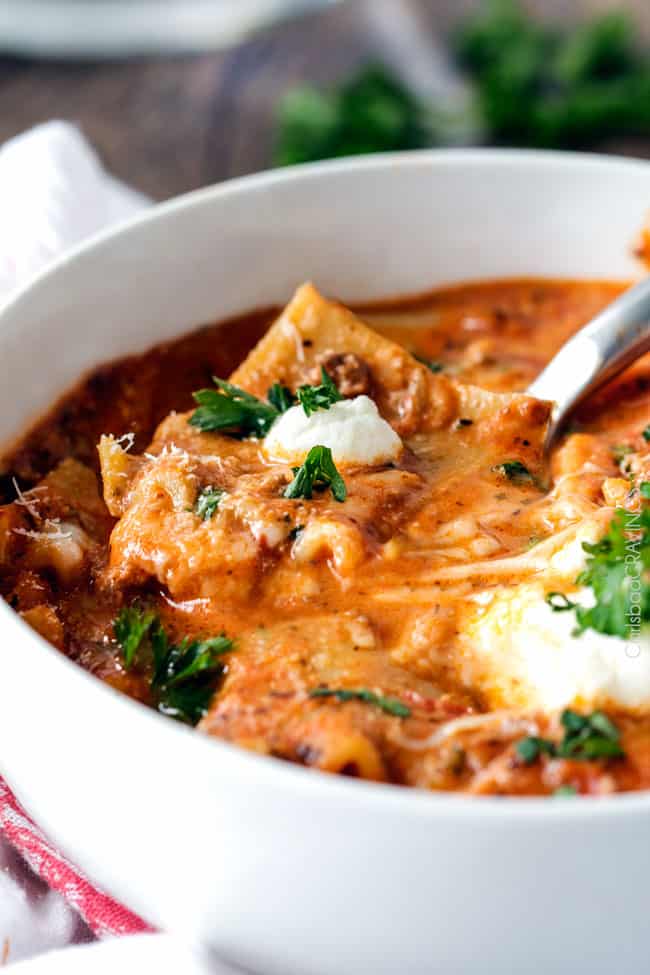 Lasagna Soup in a white bowl with cheese serving with a spoon. 