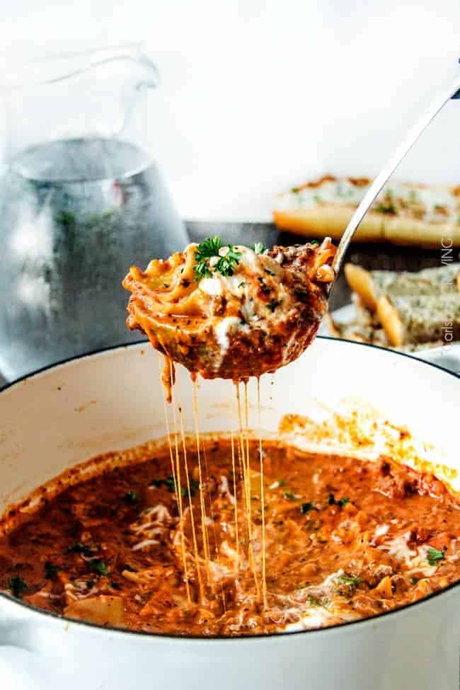 A pot of Lasagna Soup in a white bowl with cheese served with a ladle. 