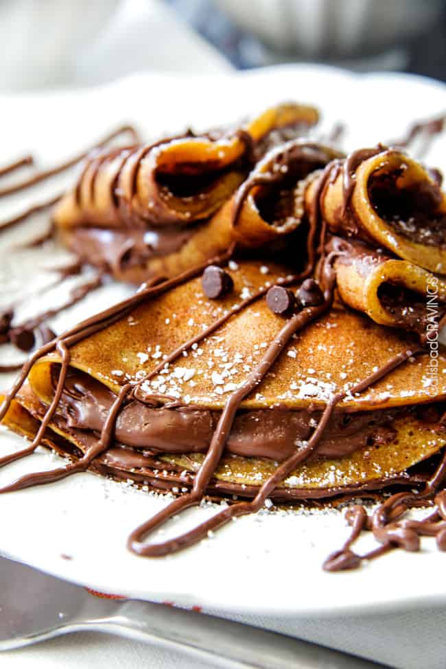 Nutella Pumpkin Crepes on a plate with powdered sugar chocolate chips and drizzle. . 