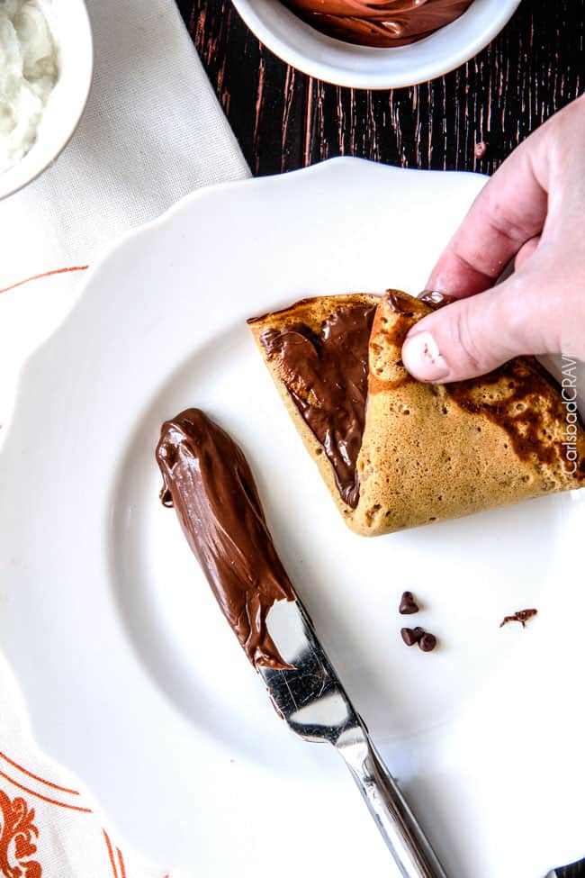 Showing how to make Nutella Pumpkin Crepes by adding nutella and folding the crepes.