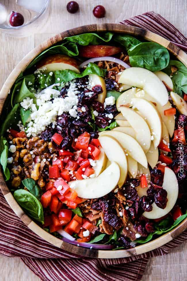 Top view of apple walnut salad in a wooden bowl with apples, walnuts, craisins, spinach, feta