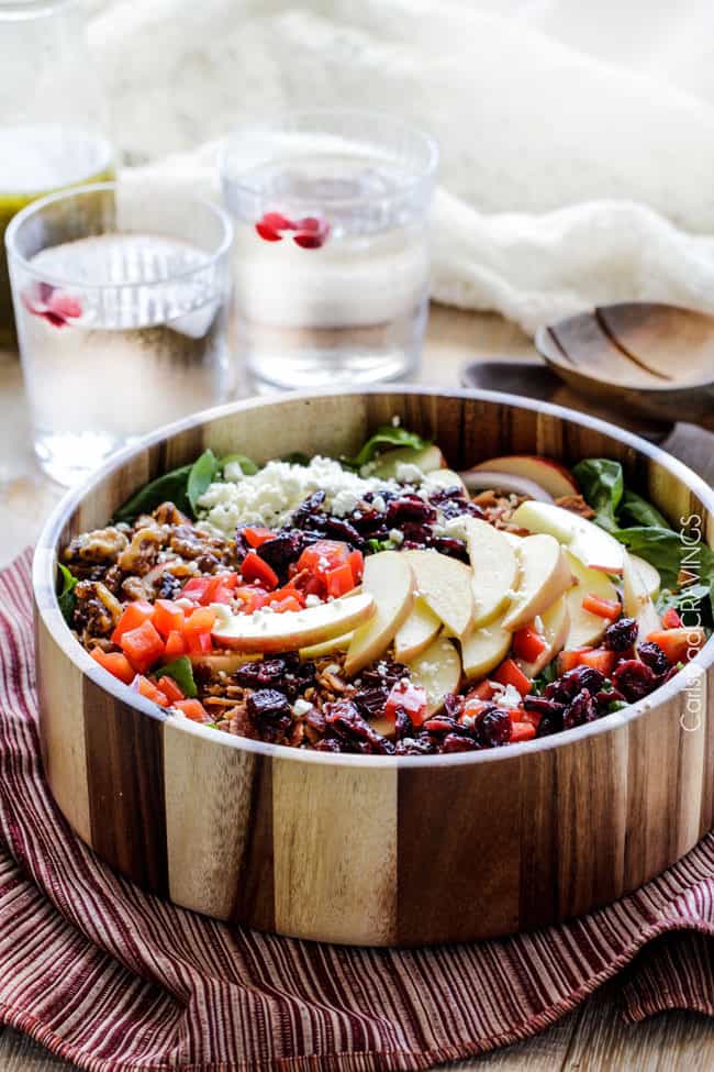 side view of showing how to make Apple Salad by adding spinach, apples, bell peppers, craisins, red onions and feta to a wooden bowl