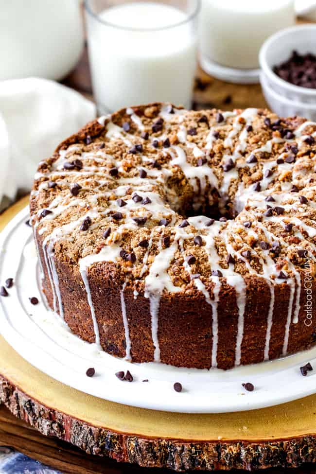 side view of sour cream coffee cake recipe with chocolate chips and vanilla glaze on a white platter