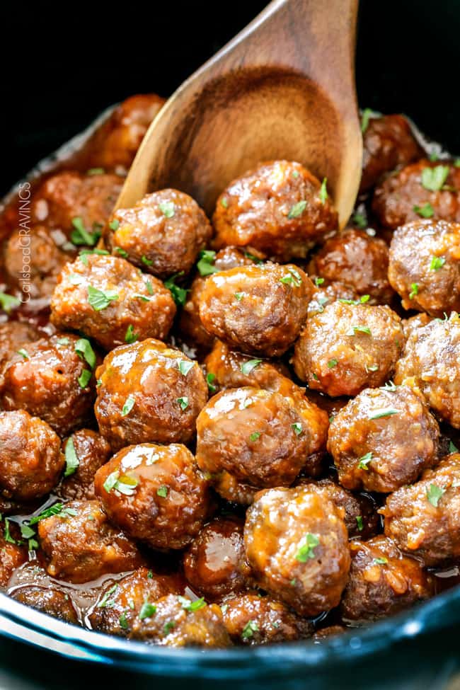 a wooden spoon scooping up buffalo meatballs in the slow cooker