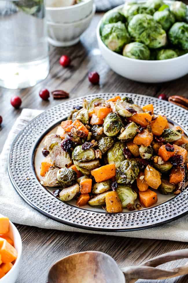 Roasted Brussels Sprouts and Butternut Squash on a black and white plate with cranberries on the side. .