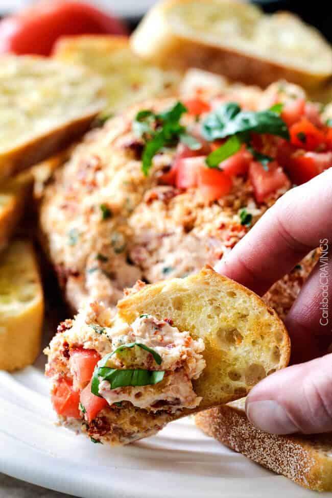 Bruschetta Cheese Ball with spread on a piece of baguette bread. 