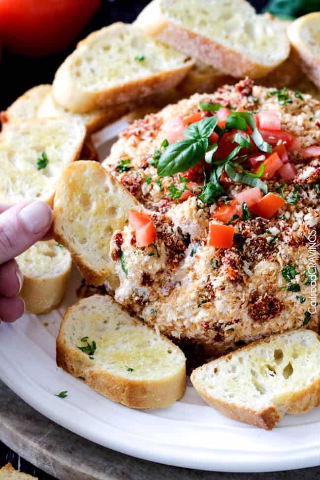Bruschetta Cheese Ball with someone dipping bread into it.