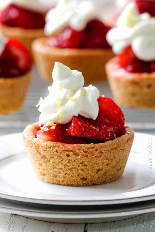 A close up of Mini Strawberry Pies with Sugar Cookie Crust with whipped cream and lemon peel zest.