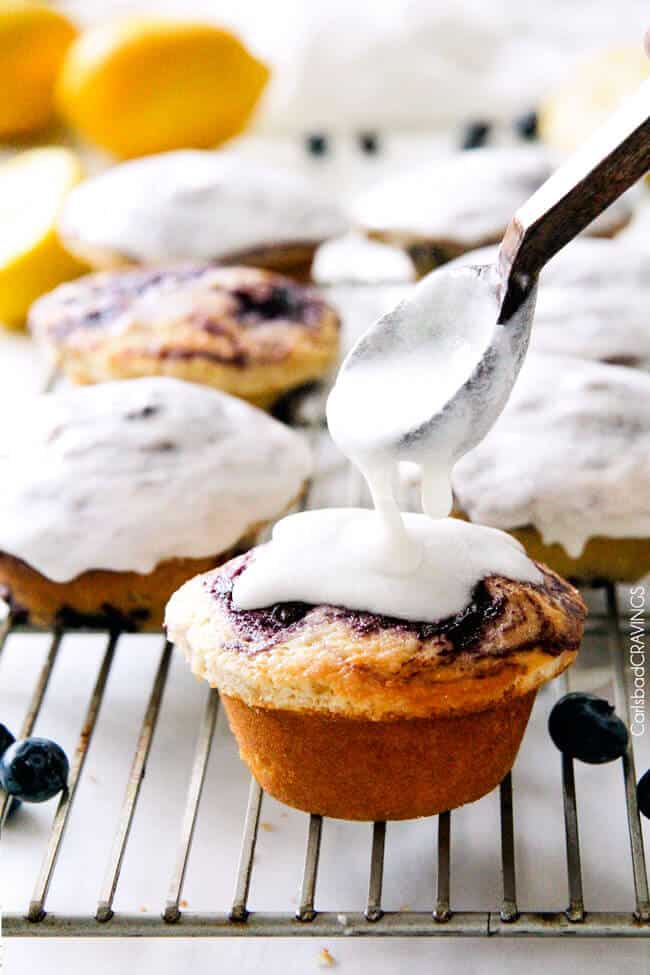 pouring lemon glaze onto the best lemon blueberry muffins on a cooling rack