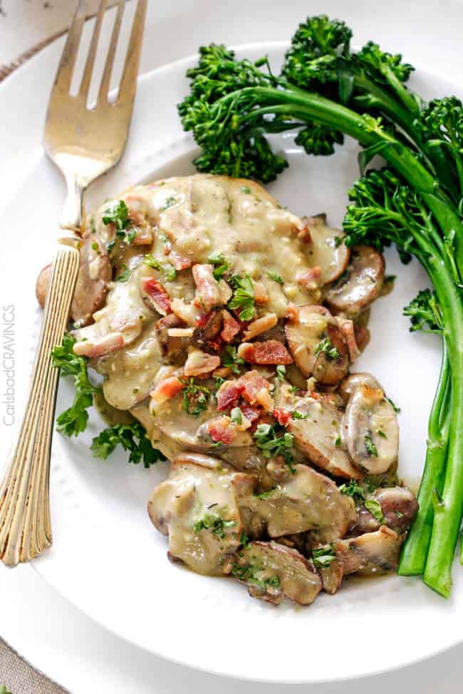serving of creamy chicken and mushroom sauce on a plate with broccolini. A fork rests on the edge of the plate. 