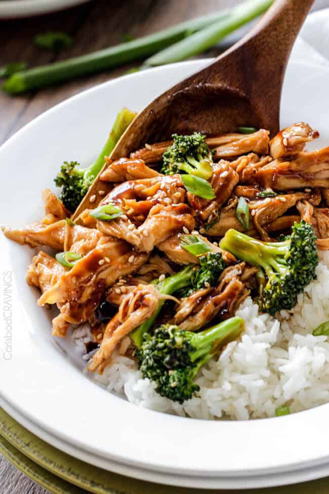 spooning mongolian chicken and broccoli onto a bed of white rice in a white bowl 