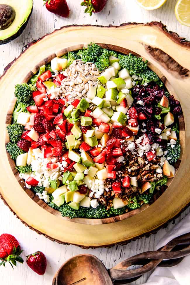 top view of best Broccoli Salad in a wood bowl on a wood platter with pears, apples, craisins, avocados, strawberries and creamy dressing