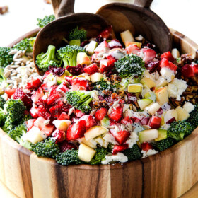 combining best broccoli salad in a wood bowl with wood tongs with creamy dressing