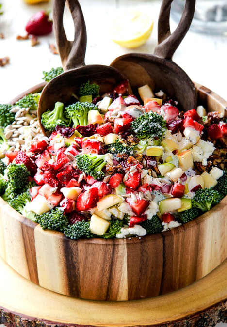 combining best broccoli salad in a wood bowl with wood tongs with creamy dressing