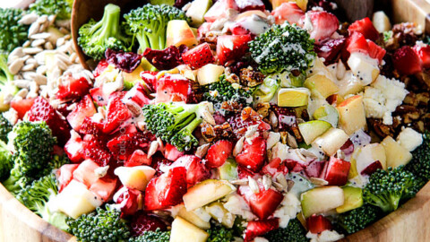 combining best broccoli salad in a wood bowl with wood tongs with creamy dressing