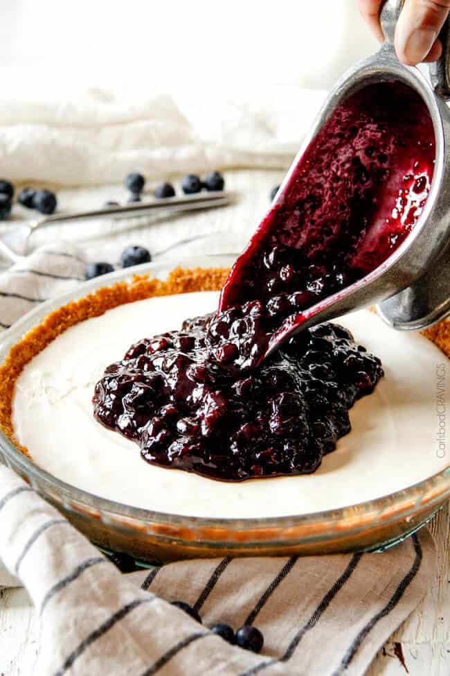 pouring blueberry cheesecake topping onto blueberry cheesecake