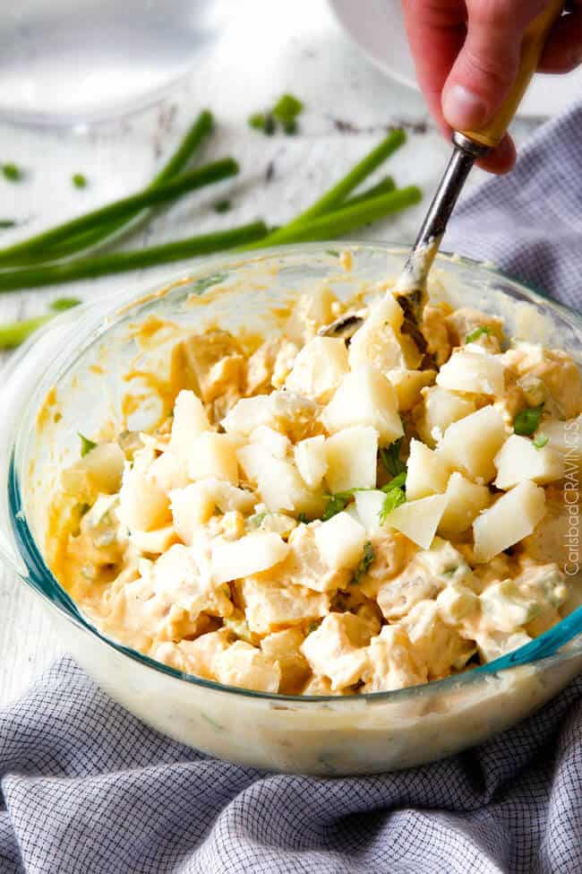 showing how to make potato salad by stirring potatoes with dressing