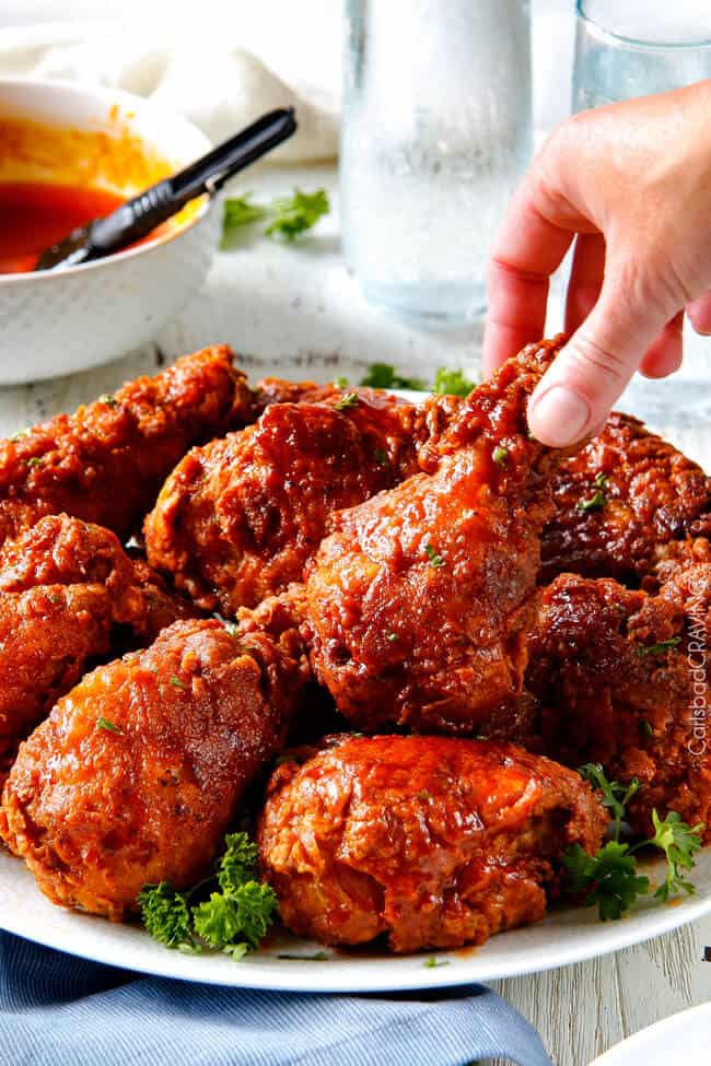 hand grabbing piece of nashville hot chicken from pile on white plate