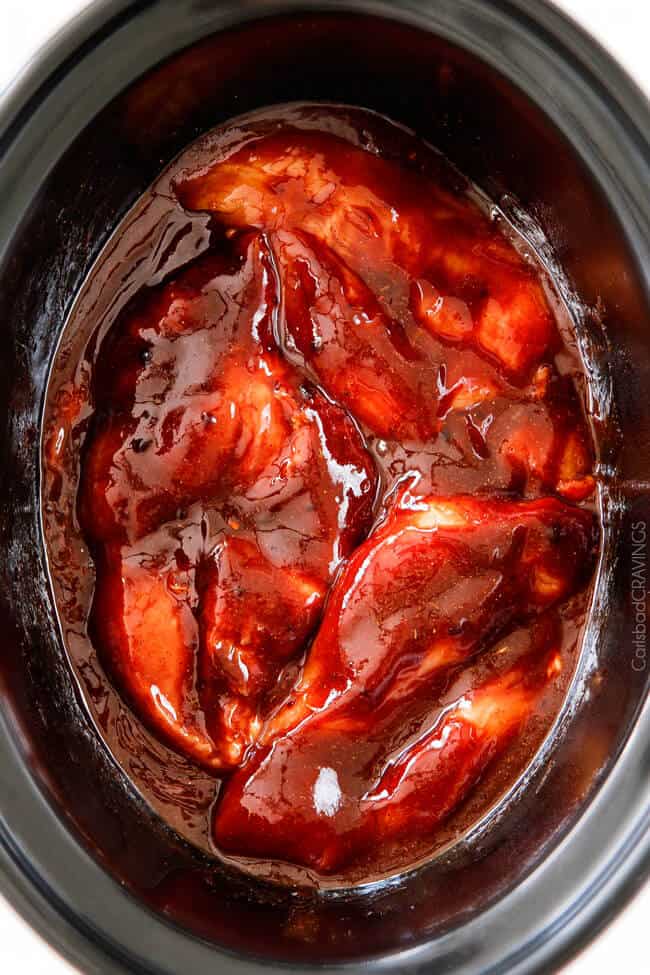 uncooked chicken breasts and bbq sauce in slow cooker insert