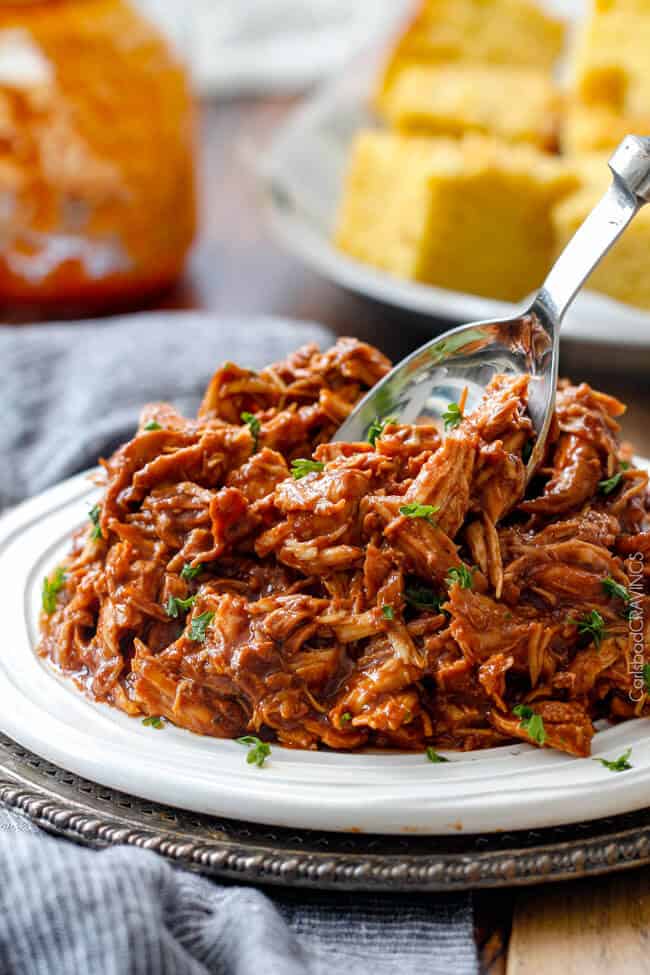 pile of crockpot shredded bbq chicken on white plate with spoon