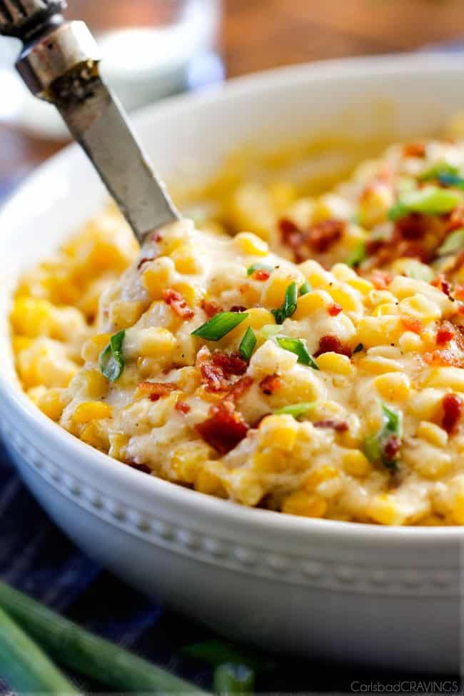 a servings spoon scooping up easy creamed corn with bacon and green onions in a white bowl