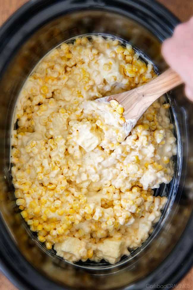 showing how to make best creamed corn by stirring corn with butter and cream cheese in slow cooker.