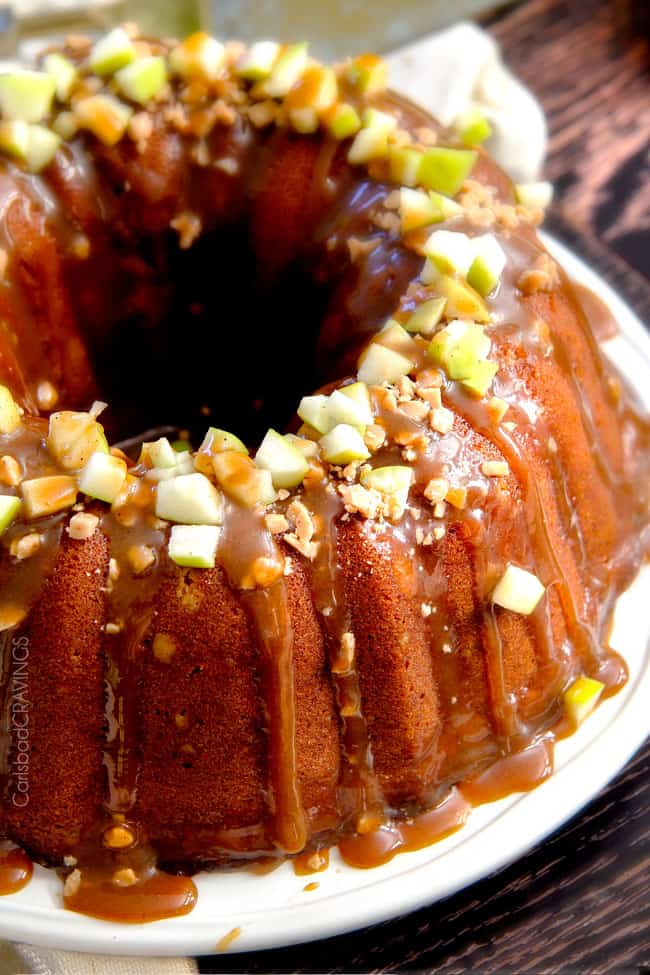 apple pound cake on a white plate. The cake is drizzled with caramel sauce and topped with toffee bits and chopped apple. 
