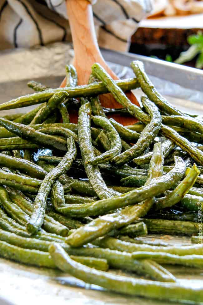 Showing how to make Roasted Green Beans with Bacon by stirring green beans on the baking sheet