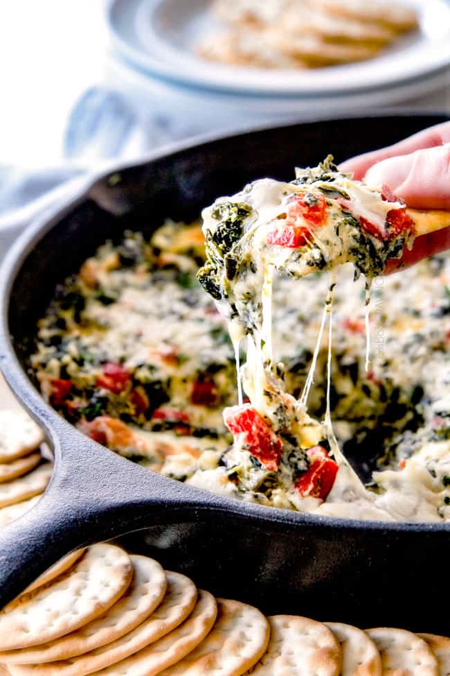pulling cracker away from baked spinach dip with lots of cheese
