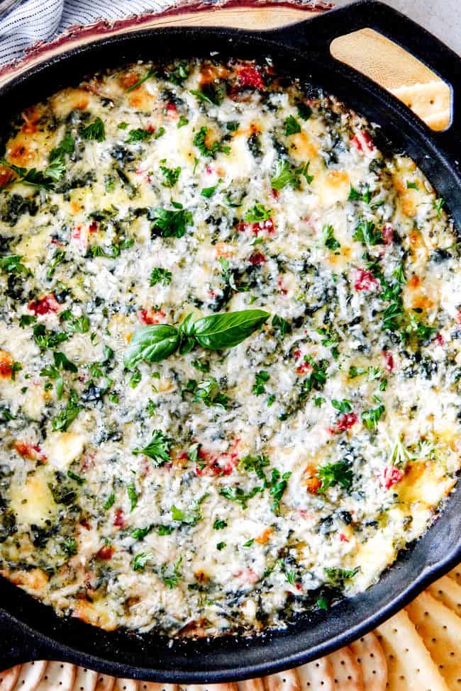 Top view of cheesy baked spinach dip with cream cheese or brie in a cast iron skillet with crackers and bread around it