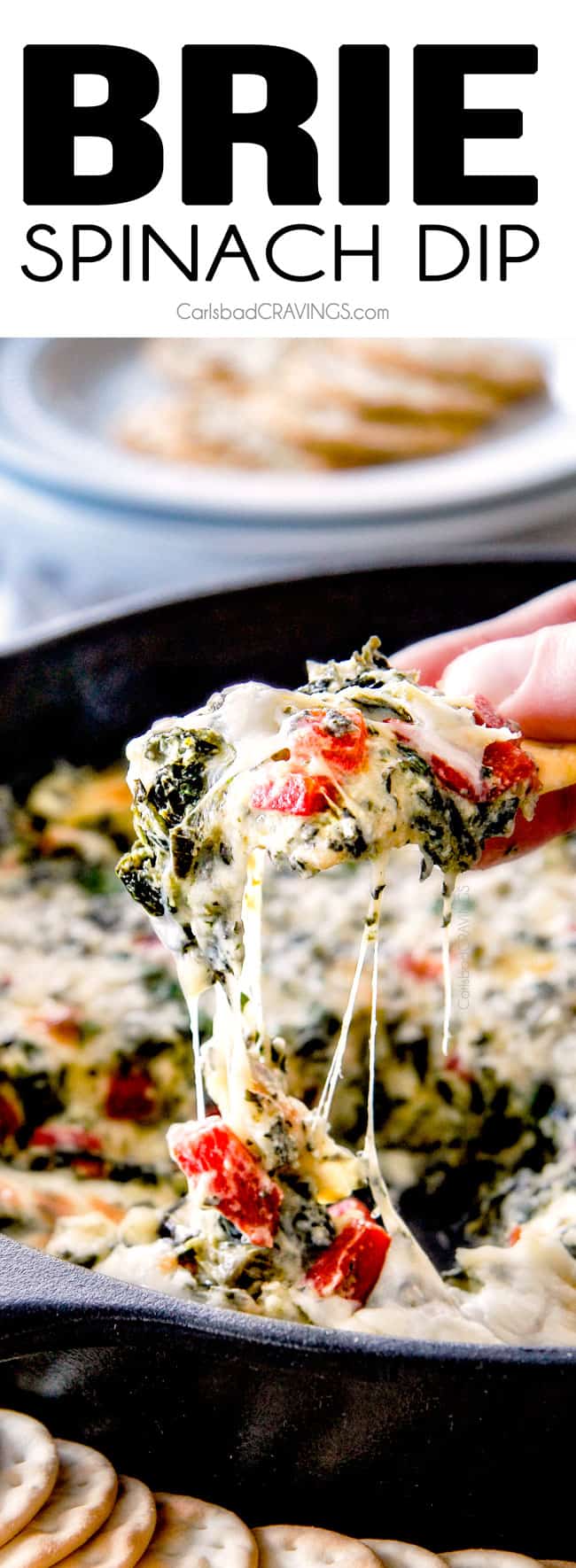 up close of a cracker pulling hot spinach dip out of a hot skillet with strings of melty cheese attached