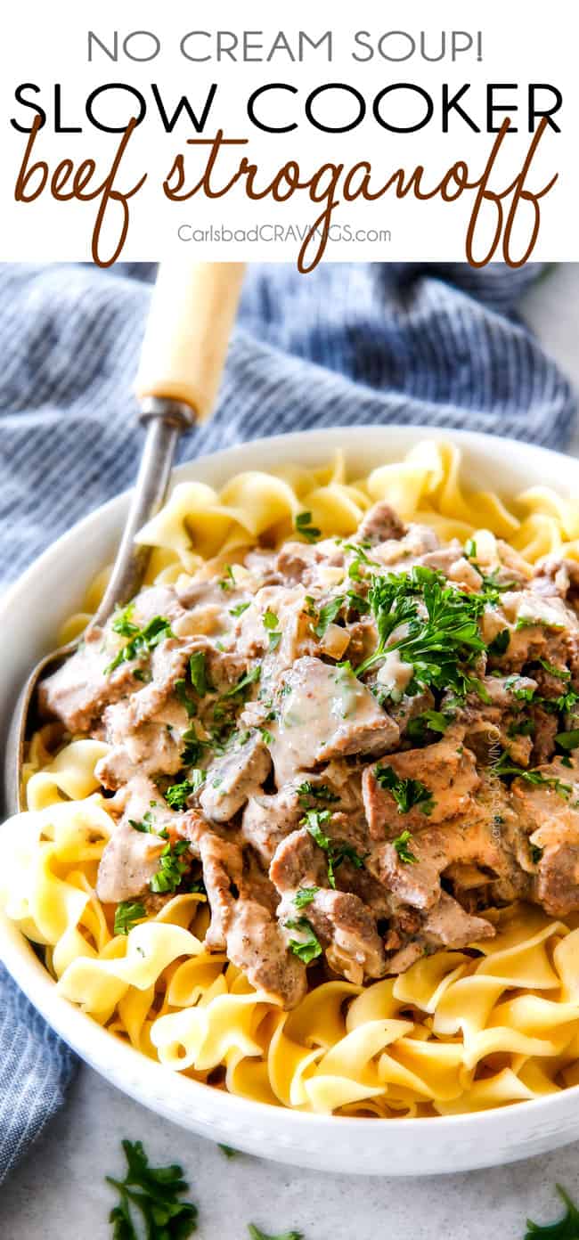 from scratch Slow Cooker Beef Stroganoff on egg noodles in a white bowl with a silver servings spoon and blue napkin