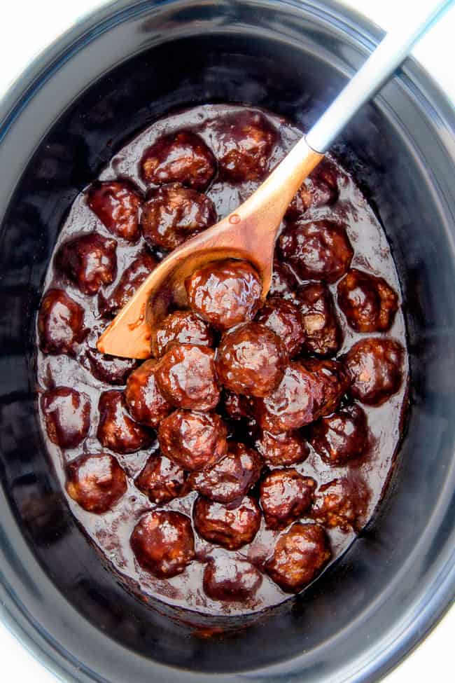 top view of crockcpot Korean Meatballs covered in Korean BBQ Sauce in the slow cooker with a wood serving spoon holding some of the meatballs 