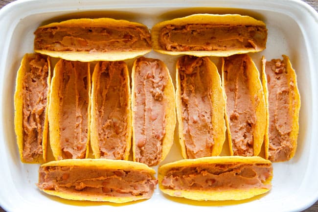 Showing how to make Ranch Chicken Tacos by adding refried beans to the taco shells. 
