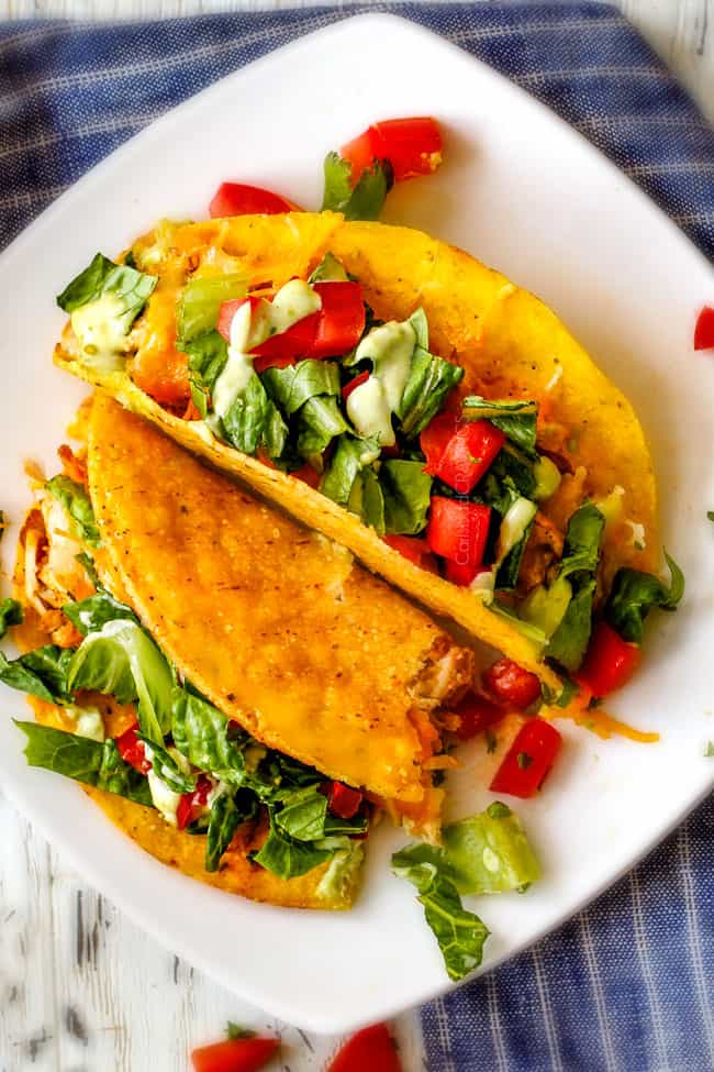 Two Ranch Chicken Tacos piled with refried beans, cheese on a plate. 