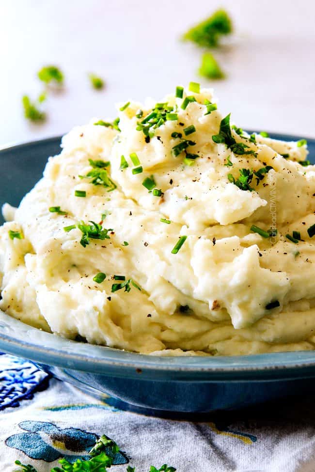 front view of a tall bowl of garlic mashed potatoes with butter, garlic, sour cream, Parmesan, chives, salt, pepper and heavy cream