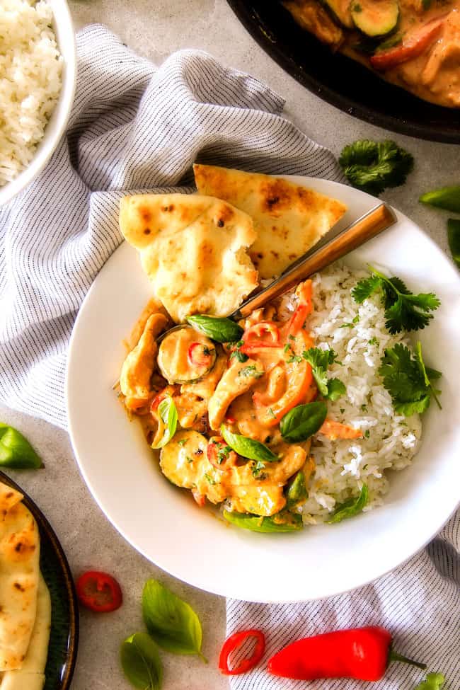 Thai Red Curry Chicken on a white plate with bread and herb garnish. 