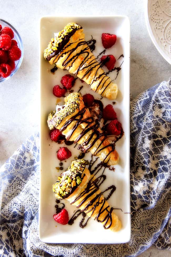 Three Puff Pastry Cannoli Cones with pistachios and chocolate on a white rectangle plate. 