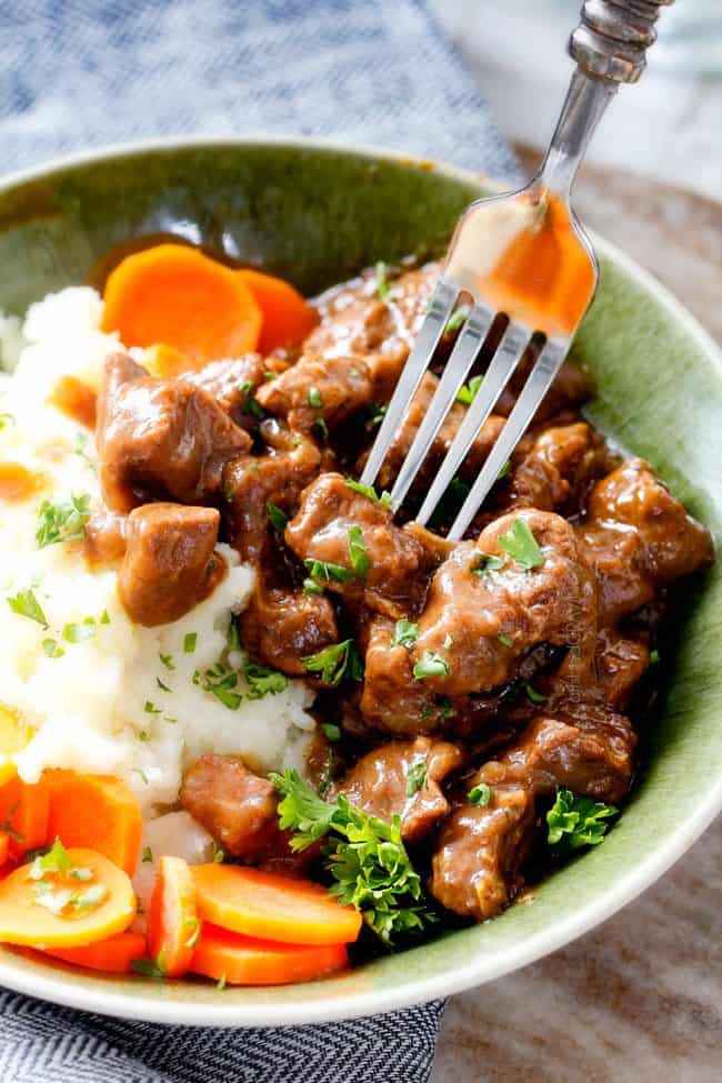 side view of beef tips, mashed potatoes, and carrots in a green bowl with a fork