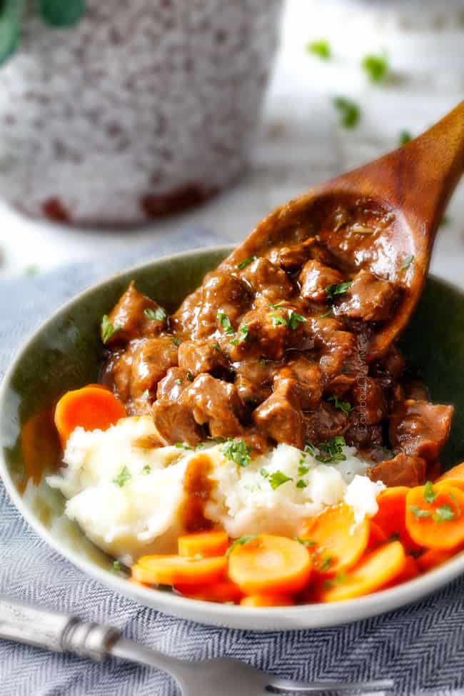 Beef Tips Recipe with gravy being served with a wood spoon onto potatoes in a green bowl