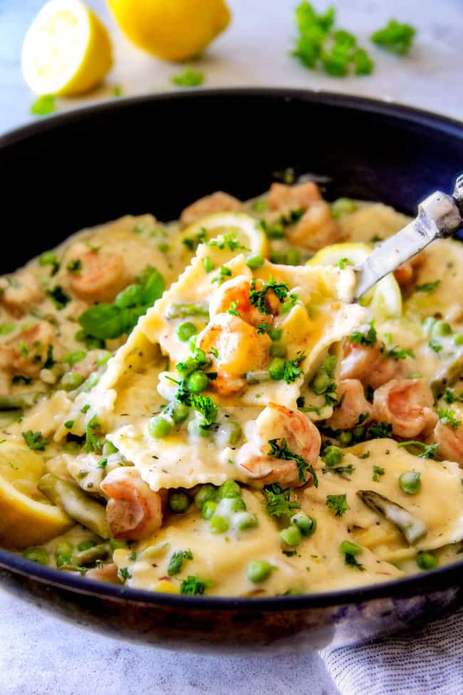 Side view of One Pot Lemon Garlic Cream Ravioli with Shrimp and Asparagus with a serving spoon.