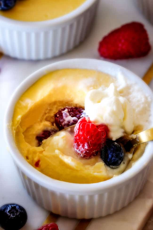 Close up vice of Lemon Pots de Creme with berries and cream on top with a spoonful missing. 