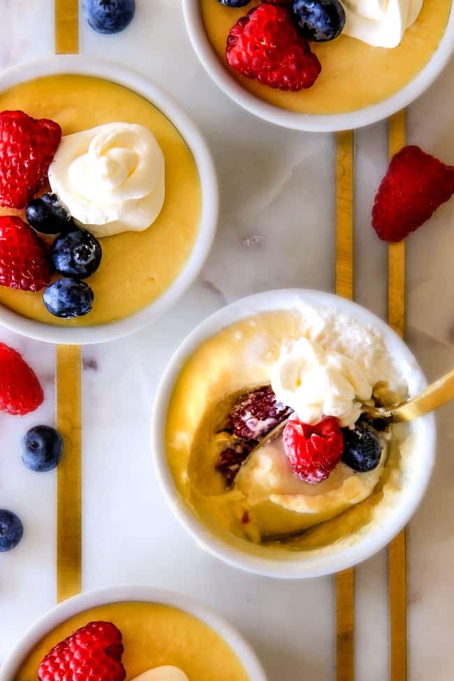 Lemon Pots de Creme with berries and cream on top with a bite missing with a spoon. 