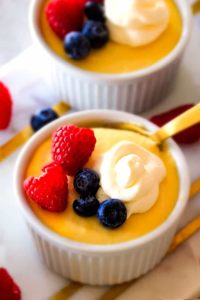 Lemon Pots de Creme with berries and cream on top with a gold spoon. 