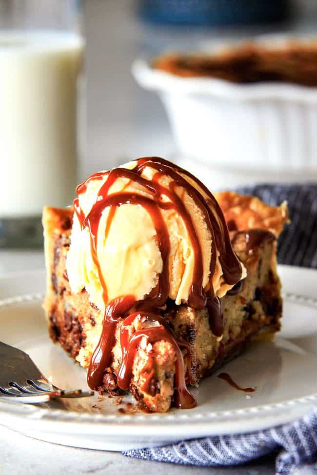 a slice of nutella cookie pie on a white plate topped with a scoop of ice cream and chocolate sauce