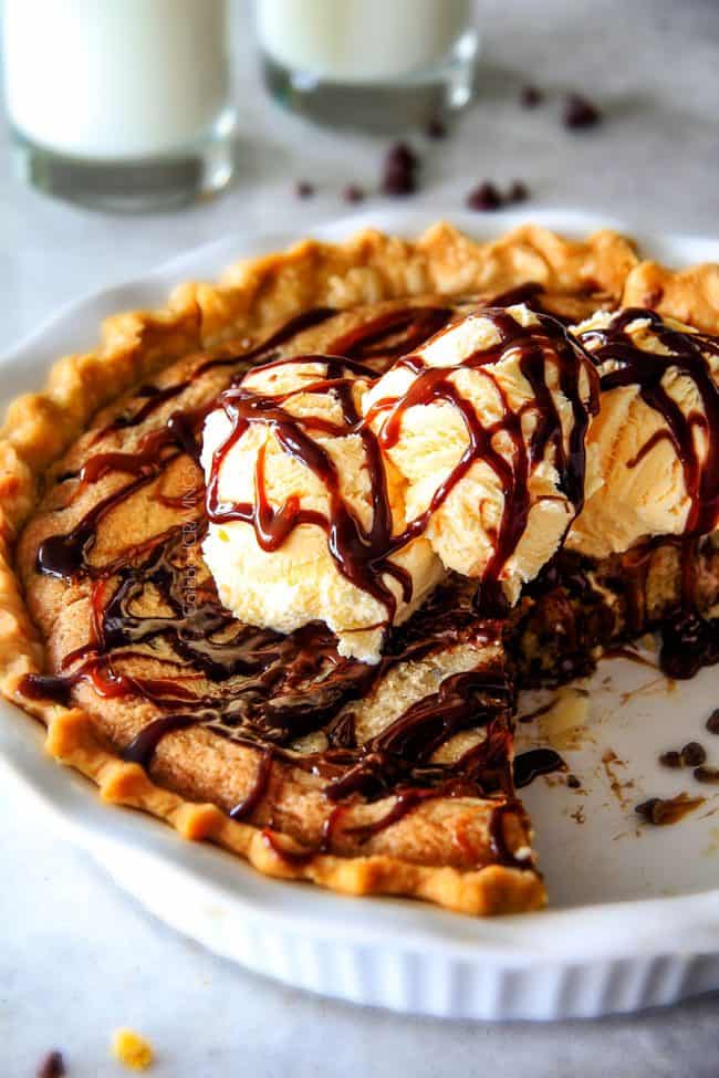 deep dish chocolate chip cookie pie in a white pie pan topped with ice cream with a few slices missing