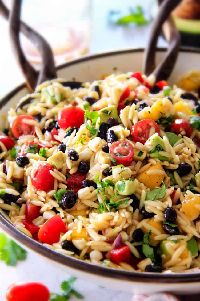 showing how to make orzo salad by tossing it in a bowl with dressing