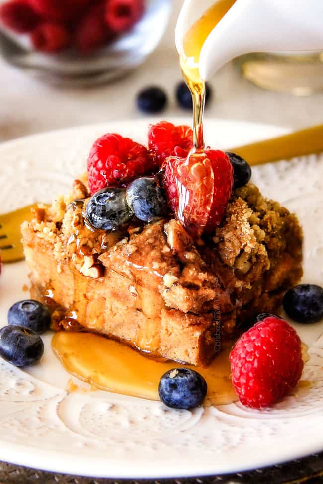 pouring syrup over Easy French Toast Casserole recipe on a white plate with berries