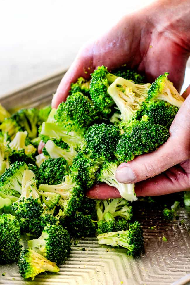 showing how to roast broccoli by tossing broccoli with olive oil on a baking sheete